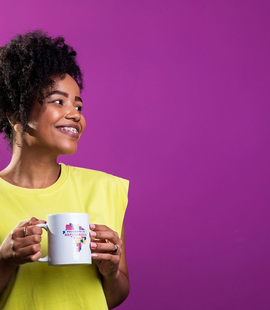 Colaboradora de camisa amarela em fundo roxo, segurando uma caneca, no escritório da Tenda Construtora. Uso institucional.