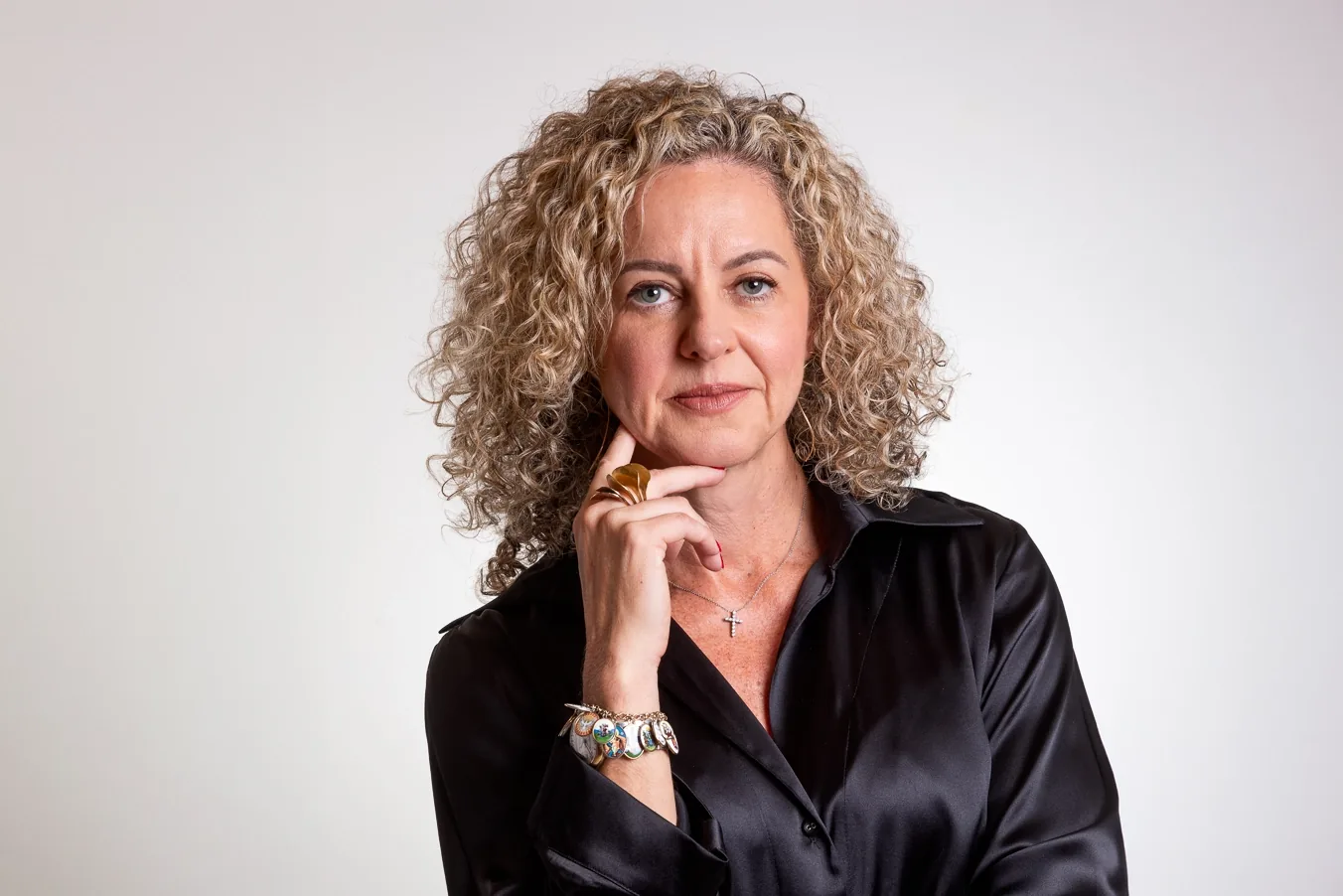 Retrato de Ana Carla Abrão, de camisa preta, com a mão no queixo, diante de um fundo claro