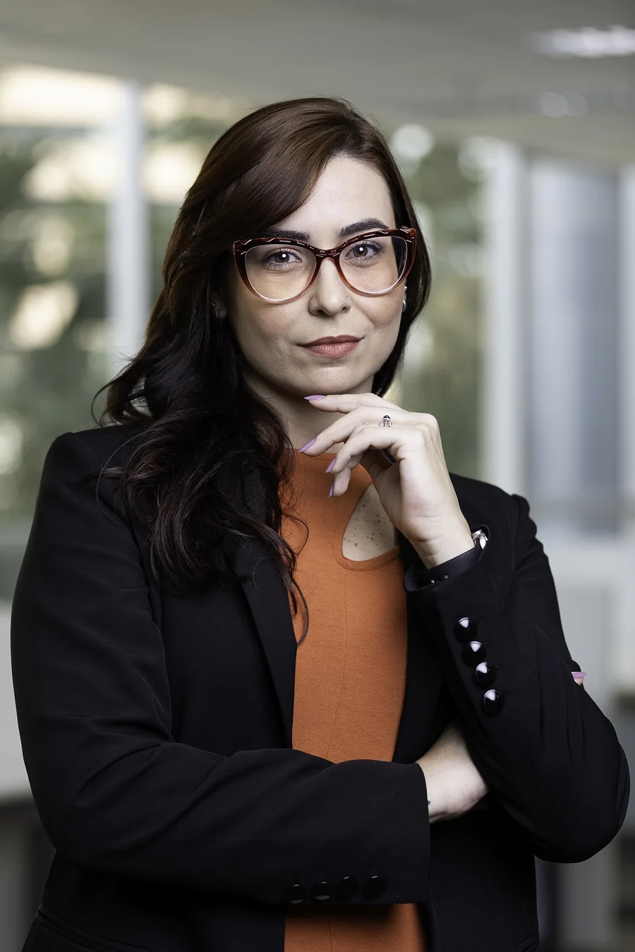Retrato de advogada com blazer preto e camisa laranja, em seu escritório