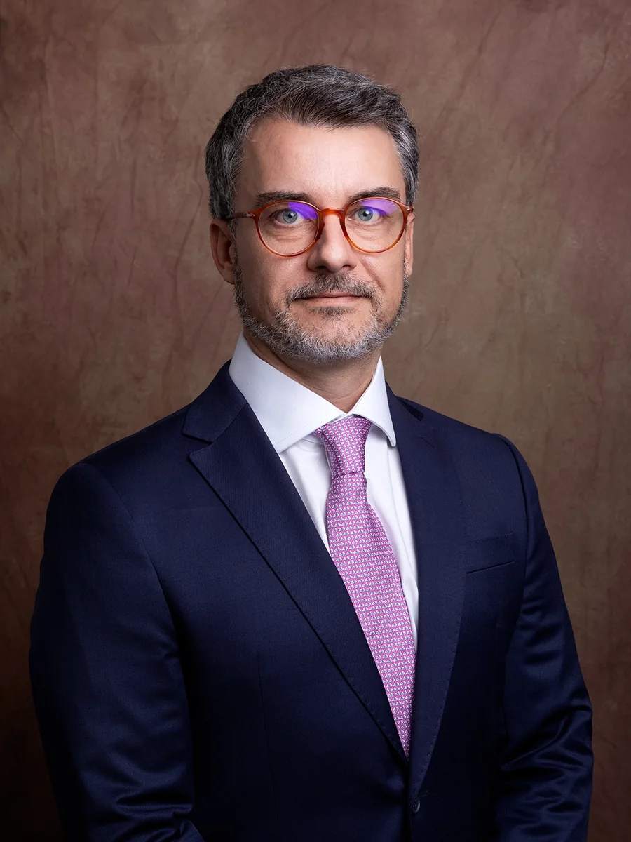 Retrato de executivo de óculos e terno azul, com fundo marrom em estúdio
