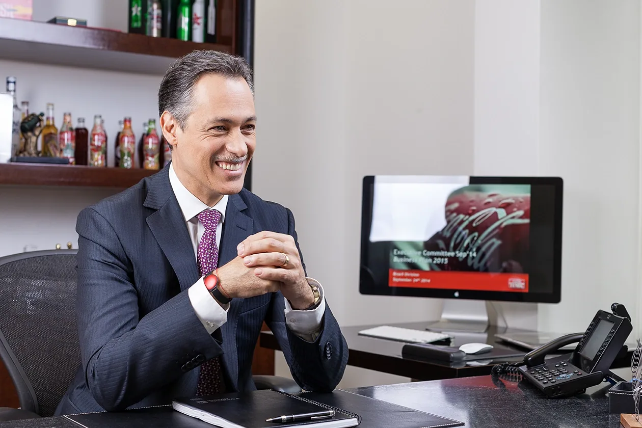 Retrato de José Ramon sorrindo, sentado à mesa de trabalho, com as mãos entrelaçadas
