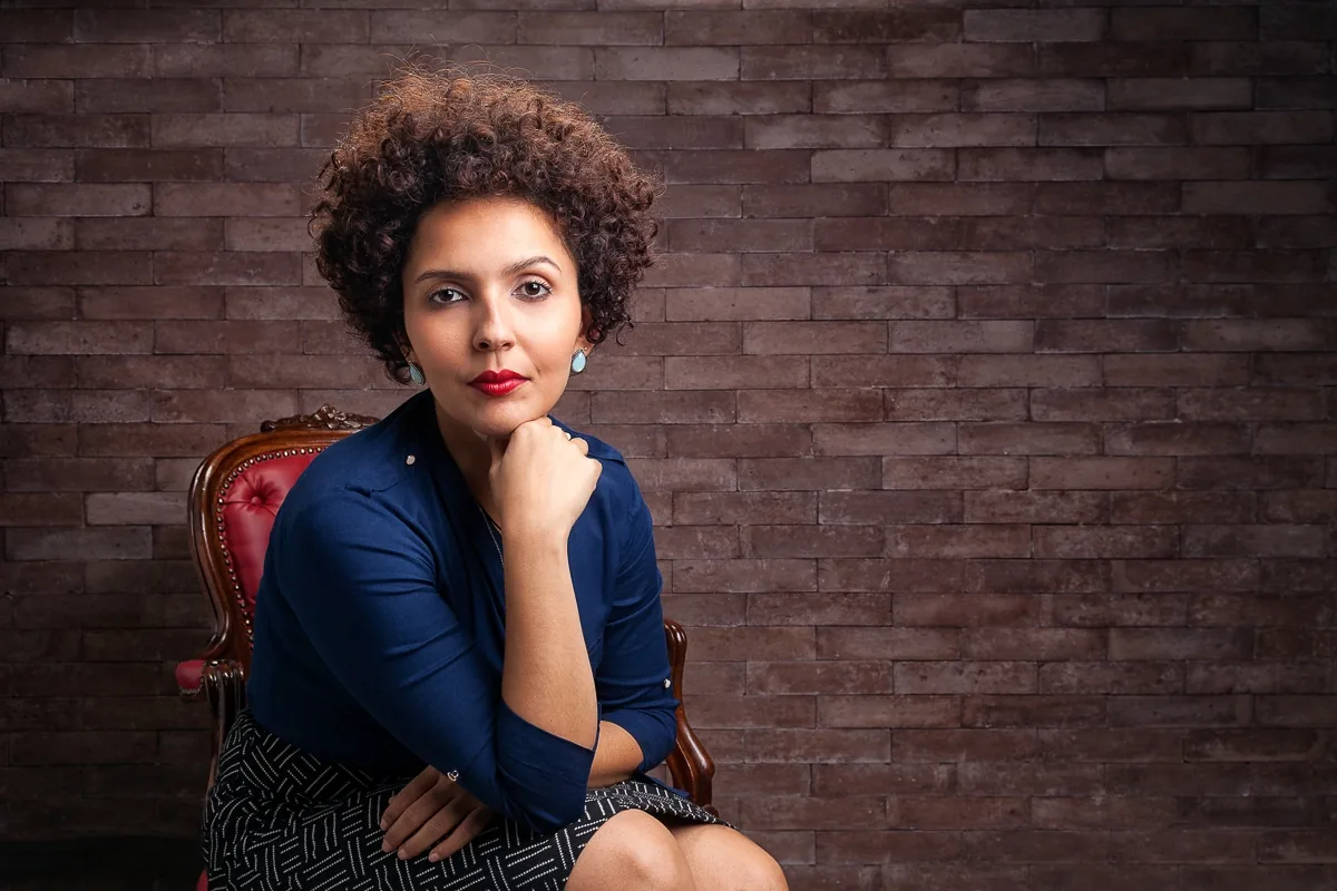 Retrato de executiva sentada diante de uma parede de tijolos